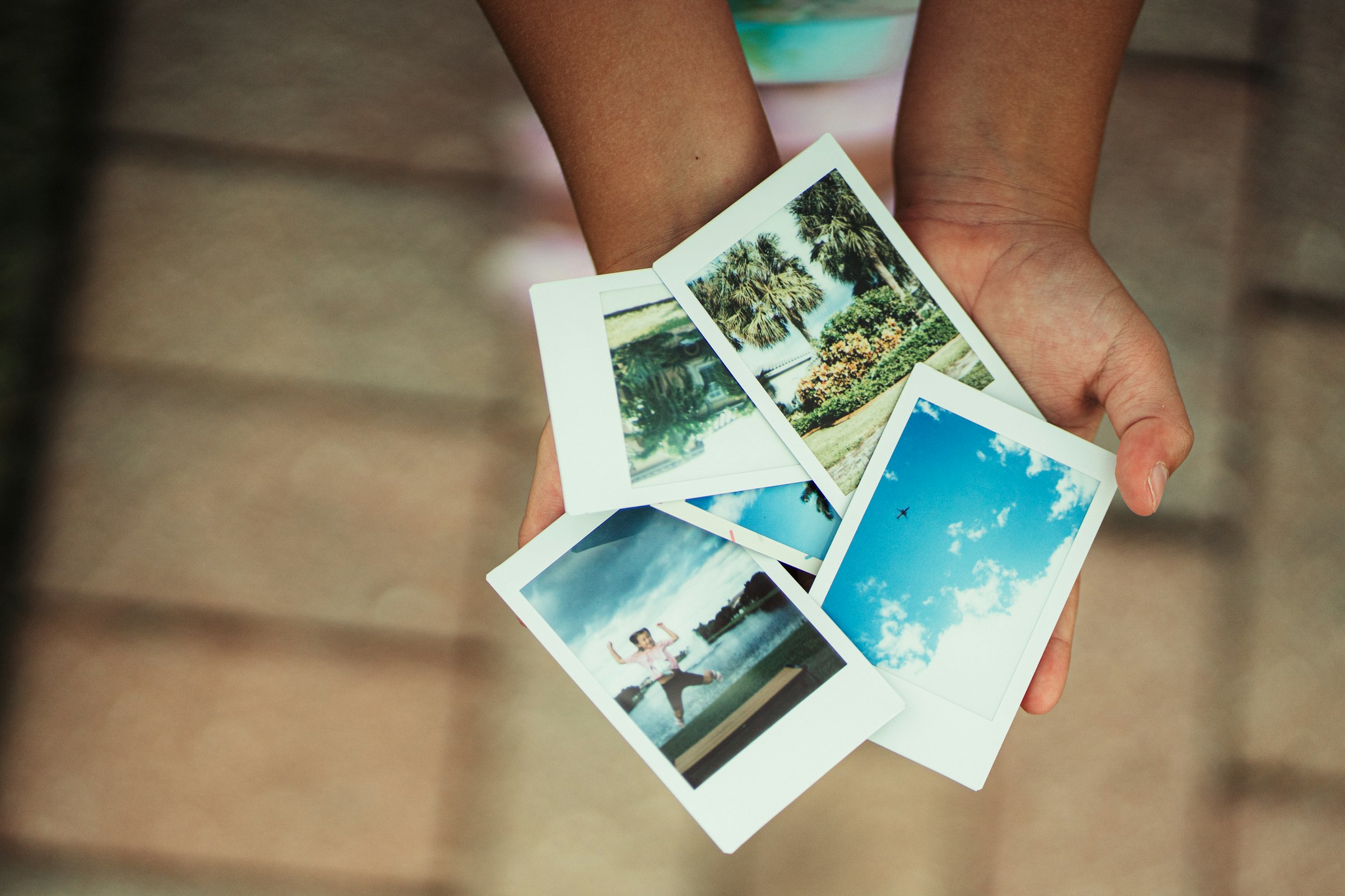 Ruky držia štyri vytlačené polaroid fotografie s letnými motívmi
