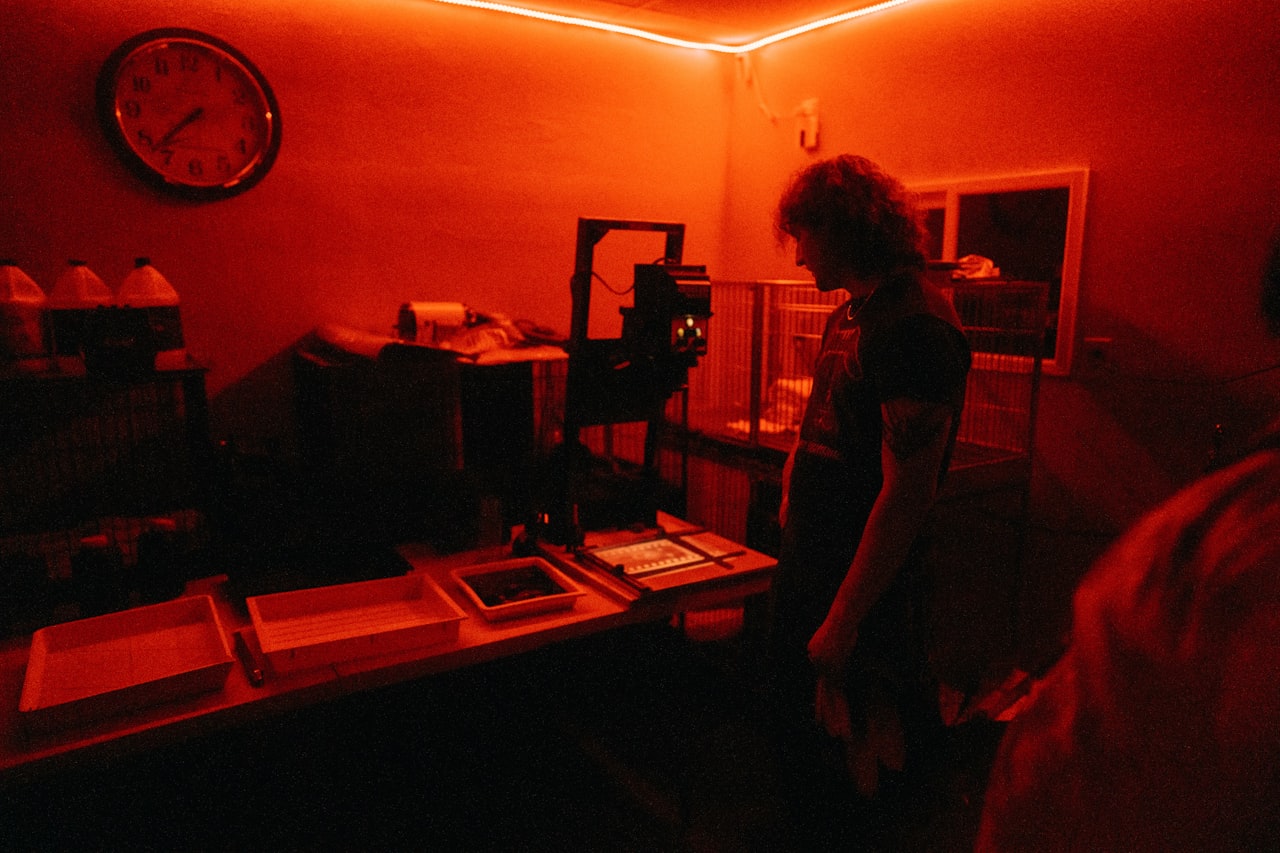 Fotograf v tmavej komore pod červeným svetlom pri spracovaní fotografie